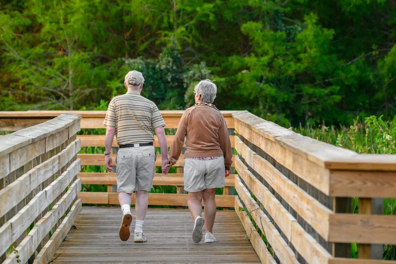 Una pareja mayor camina tomada del brazo por un sendero de madera